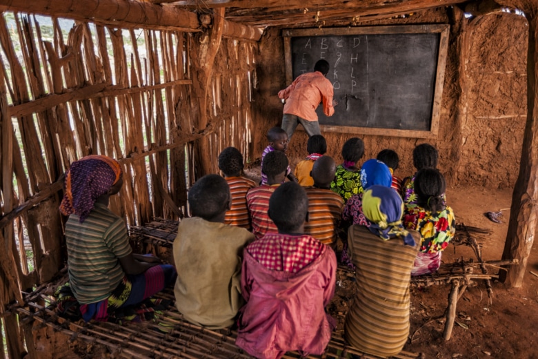 African children during english class in very remote school. The bricks that make up the walls of the school are made of clay and straw. There is no light and electricity inside the classroom
